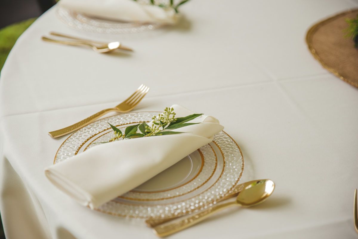 Place setting with a folded white napkin, gold flatware and a sprig of greenery