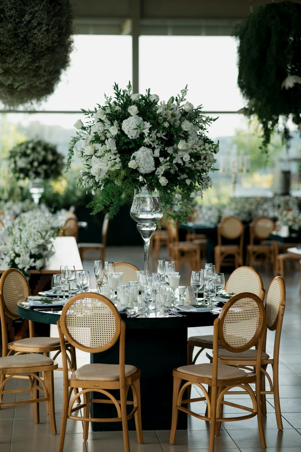 Reception table with a tall white floral centerpiece and gold chairs